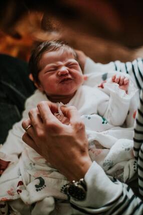 Photo of a newborn baby with a scrunched up face in the lap of parent.